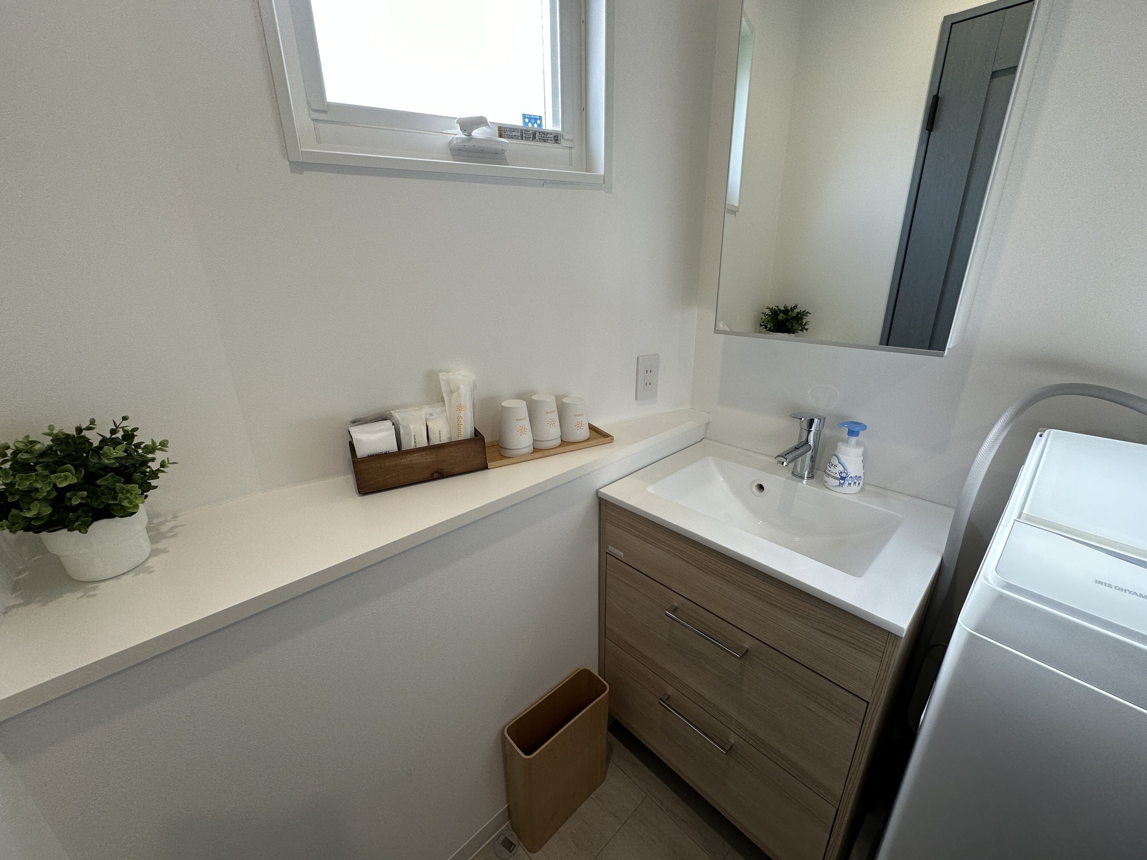 A bathroom with a white sink, wooden vanity, and a small window.