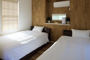 Ein Hotelzimmer mit zwei Einzelbetten, einem Holzkopfende, einer Wand-Klimaanlage, einer digitalen Uhr und einem kleinen Regal mit einer Pflanze.