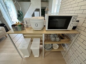 Une cuisine équipée d’un four à micro-ondes, d’une machine à café et d’une plante suspendue. On y trouve des placards de rangement et un plan de travail avec des ustensiles.