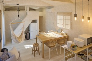 Un espacio habitable compacto con una hamaca, una zona de comedor con mesa y sillas, una kitchenette y un microondas.