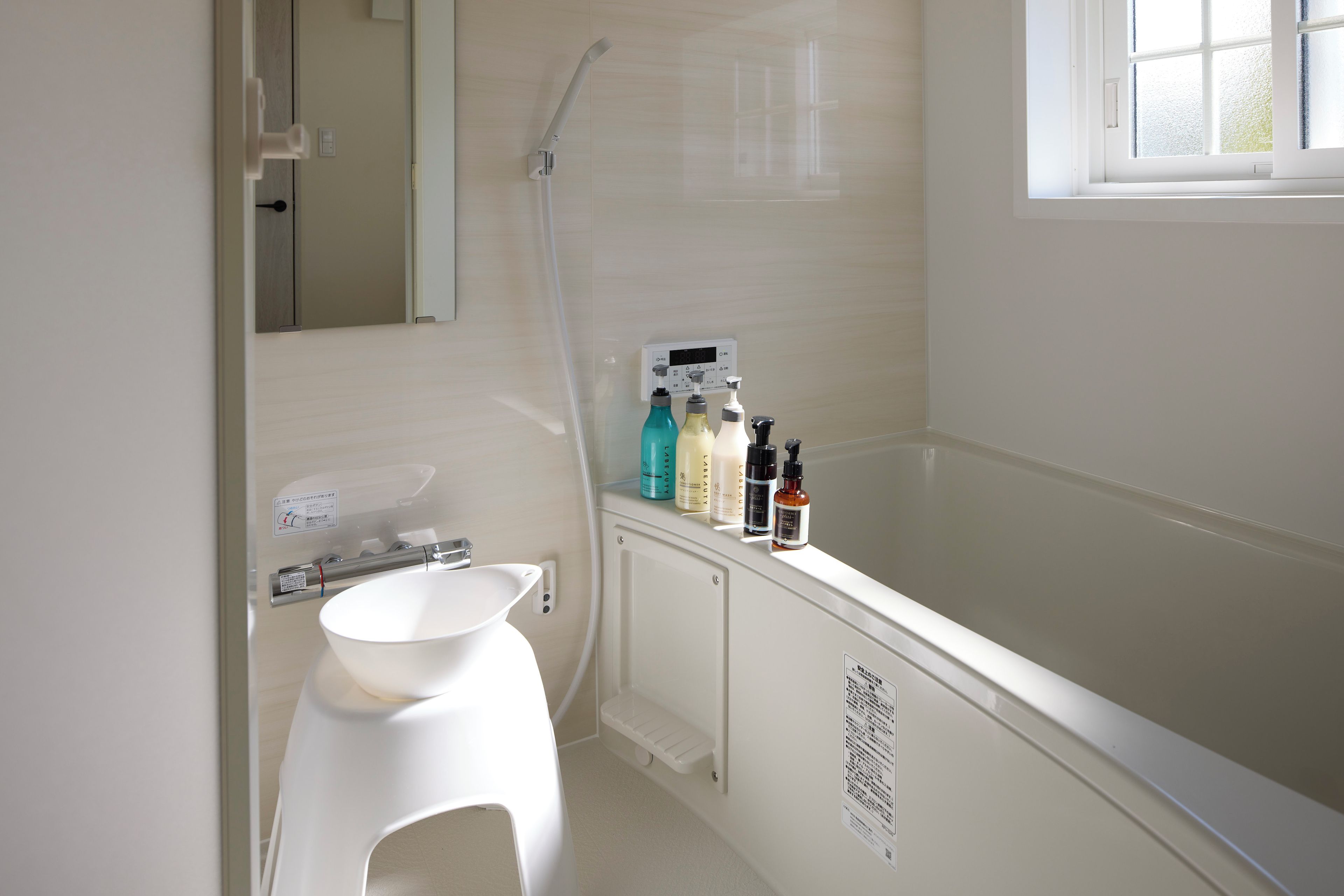 A bathroom with a white sink, a mirror, a shower, and a window.