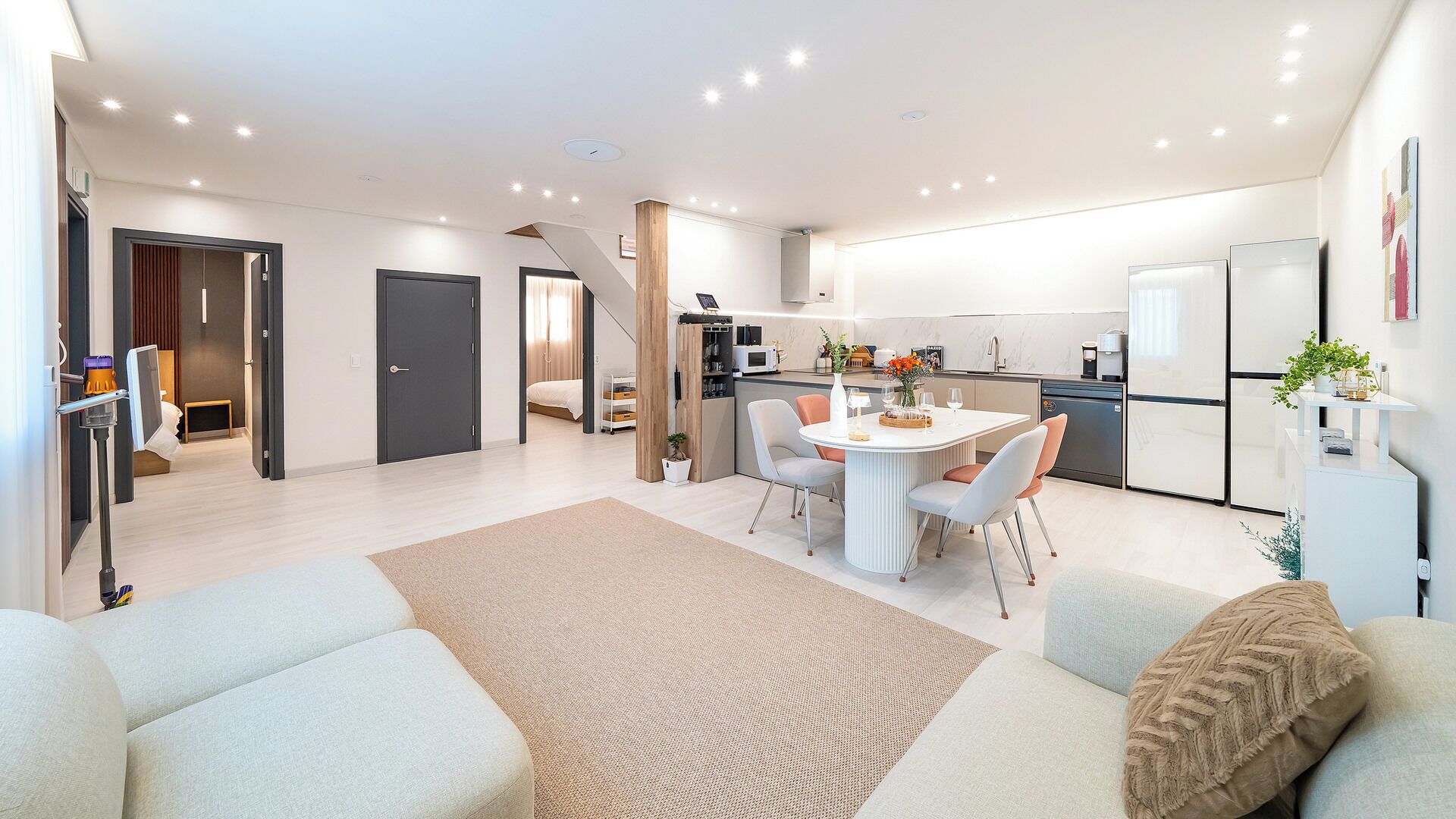 A modern living room with a dining area, a kitchen, and a staircase leading to another level.
