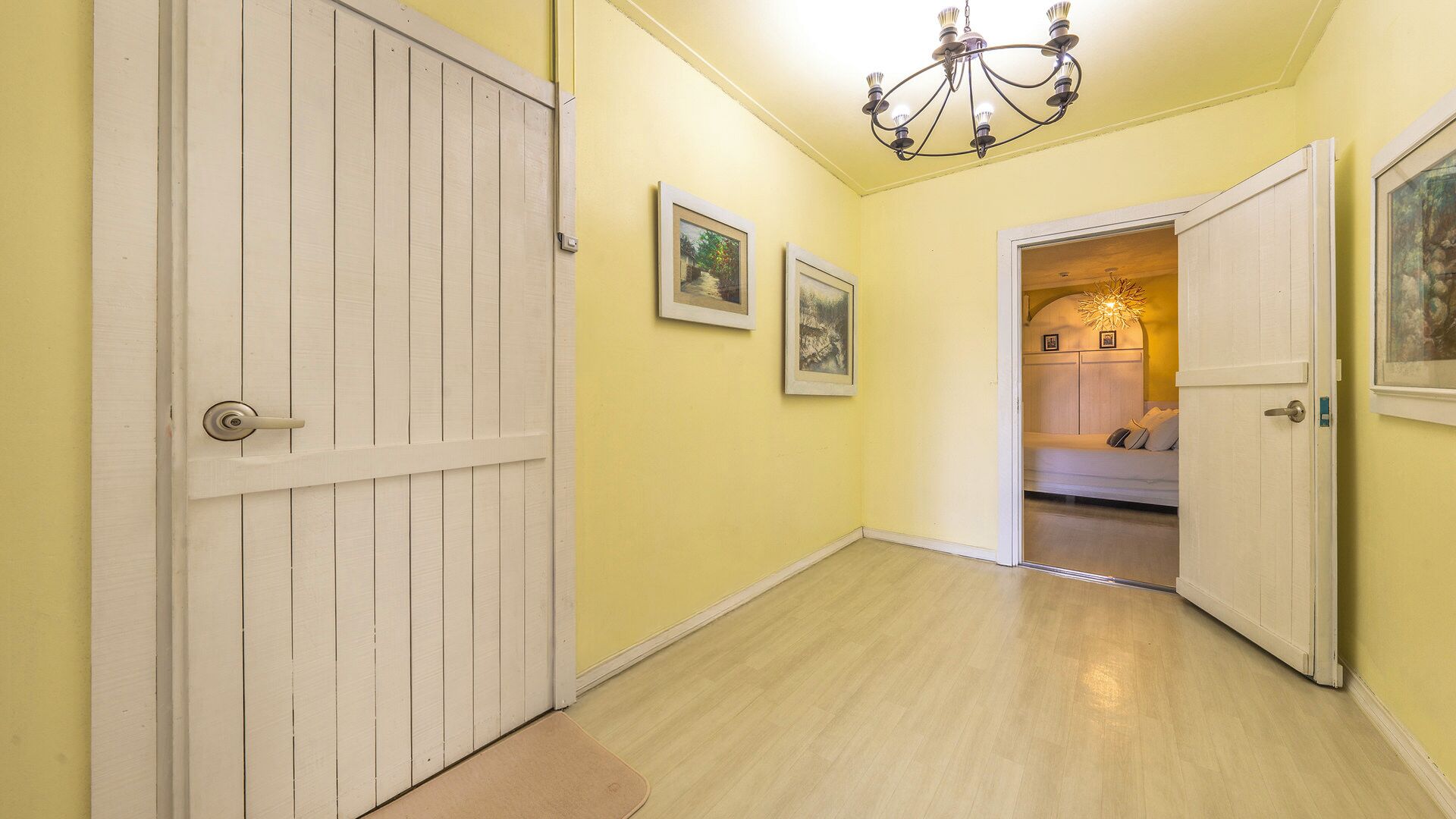 A hallway with a white door, a chandelier, and framed pictures on the wall.
