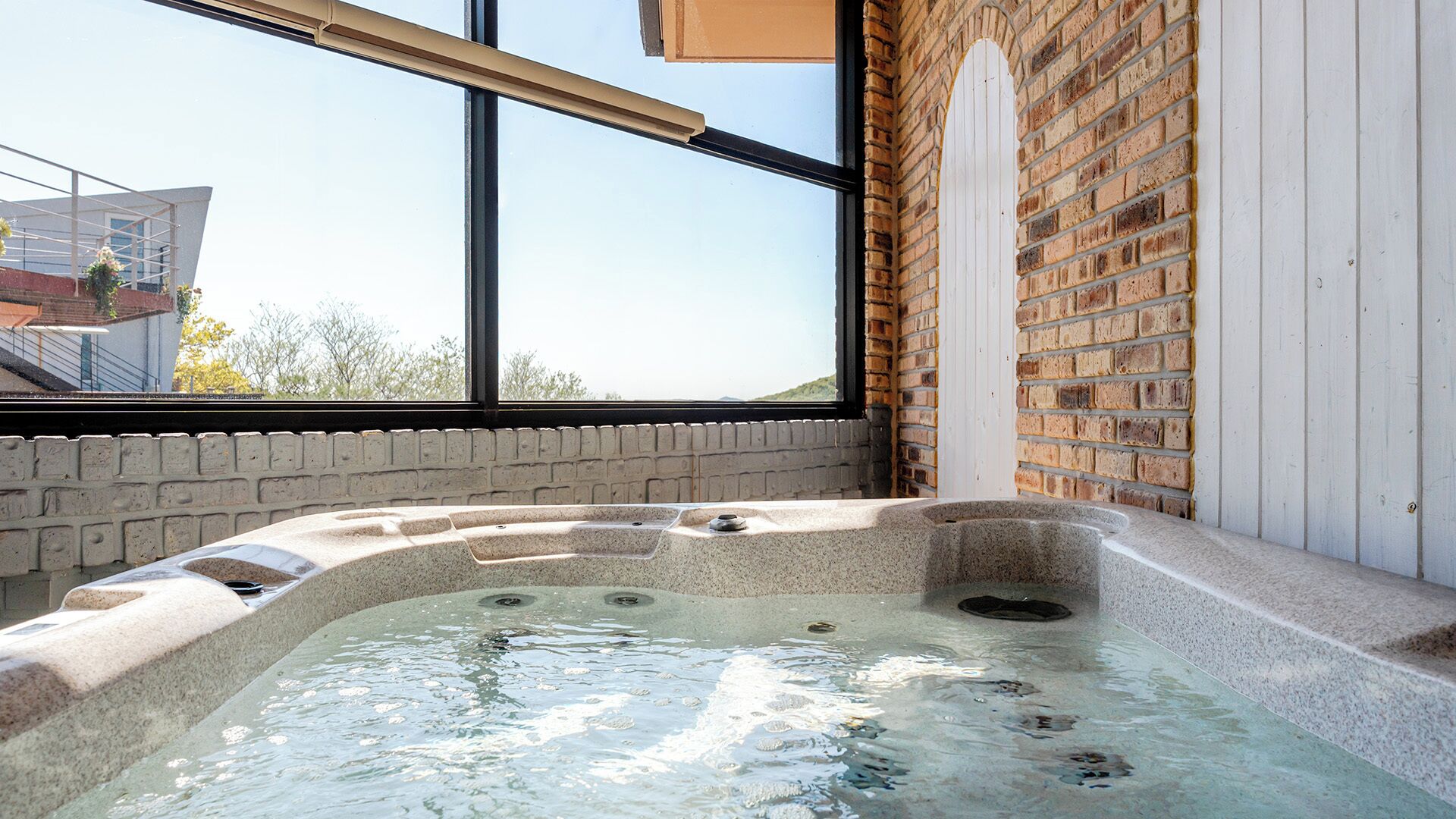 A hot tub with a view of a brick wall and a window.