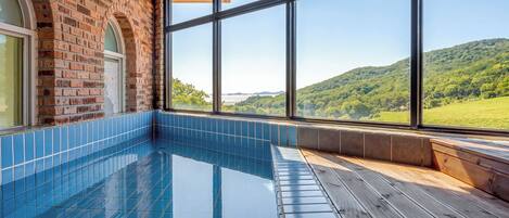 A swimming pool with a view of a green landscape through large windows.