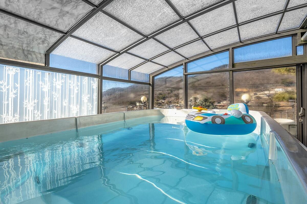 Una piscina con cerramiento de vidrio, un jacuzzi y vistas al exterior.
