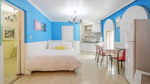 Una habitación con una cama, una mesa de comedor con sillas, una zona de cocina y un refrigerador.
