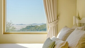 A bedroom with a bed, a window with curtains, and a view of a landscape. - Ganghwa Sky Garden Poolvilla (Incheon)
