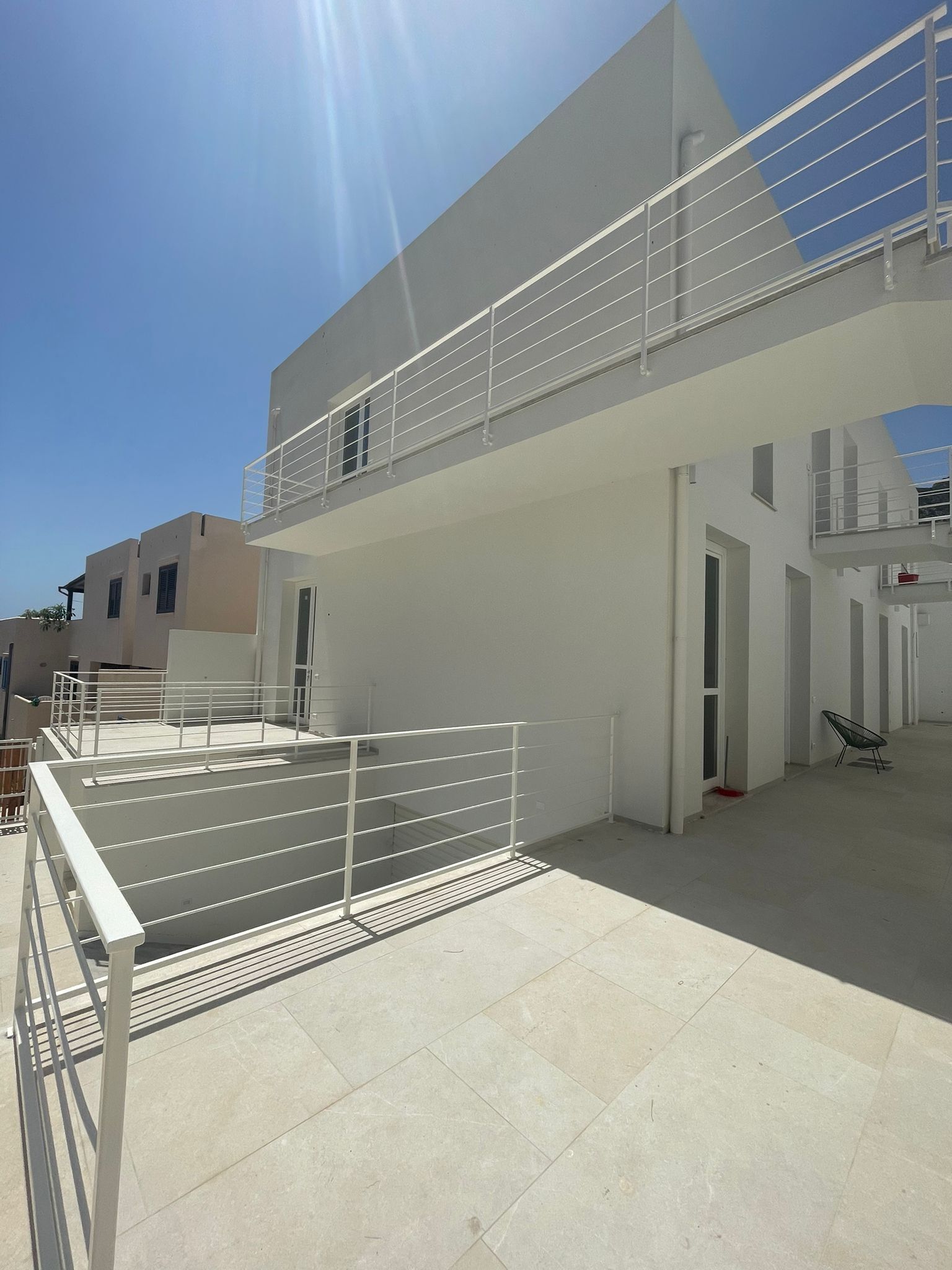 Un bâtiment moderne doté d’un toit plat, d’un balcon avec une rambarde en métal et surplombant un ciel dégagé.