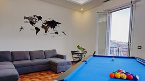 Ein modernes Wohnzimmer mit Billardtisch, einem grauen Ecksofa und einer Weltkarte an der Wand.
