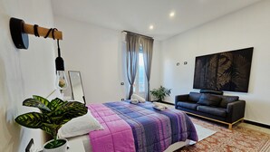 Ein modernes Schlafzimmer mit Bett, Nachttisch, Lampe, Topfpflanze und einem großen Bild an der Wand.