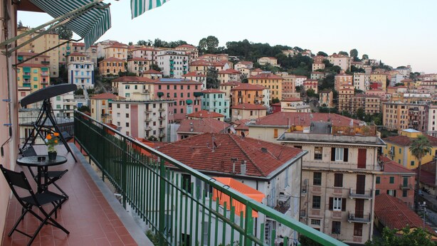 Ein Balkon mit Tisch und Stühlen mit Blick auf einen dicht bebauten Hang voller farbenfroher Häuser.