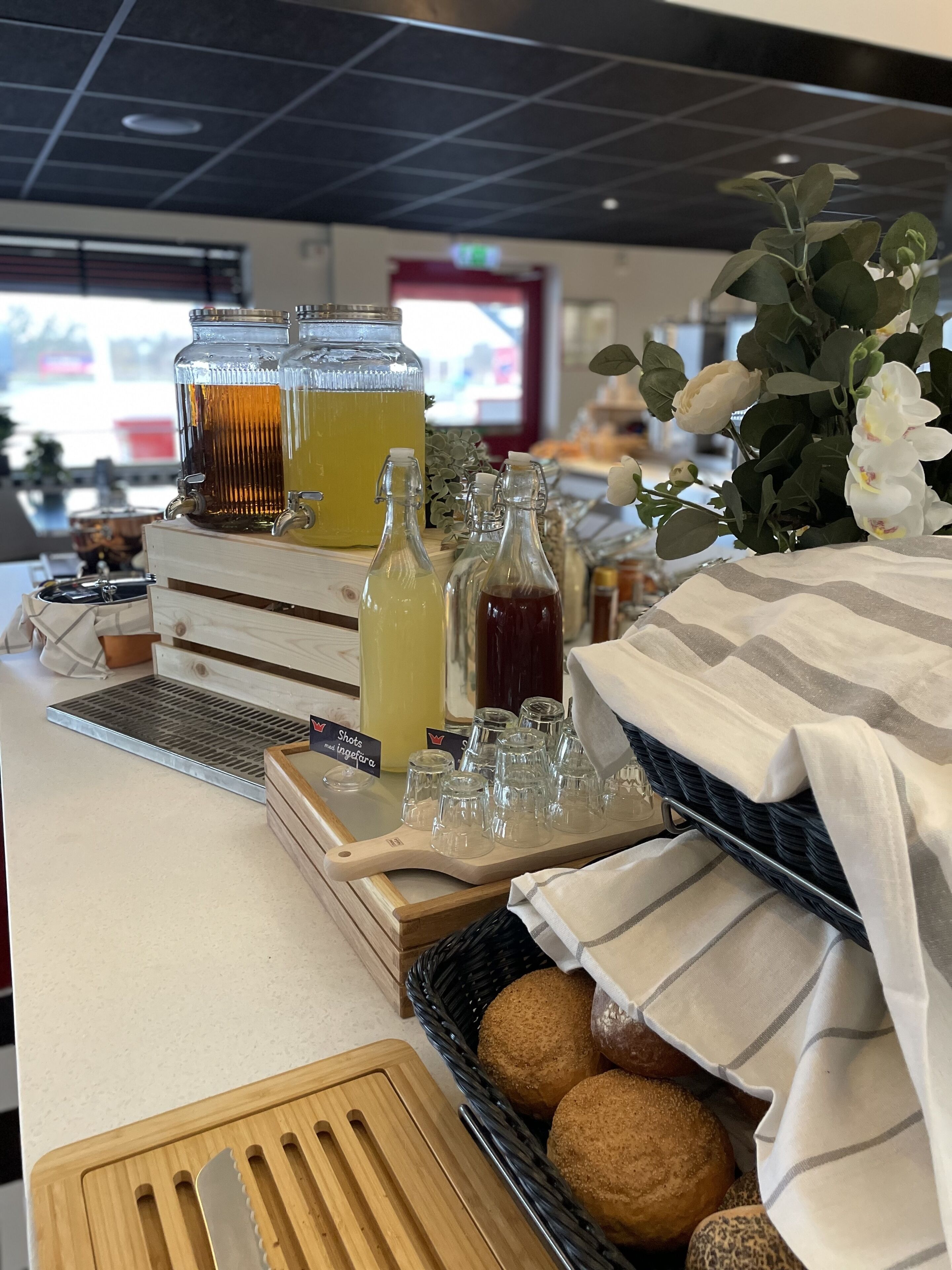 Un buffet pour le petit-déjeuner avec diverses boissons, un plateau de pains et une plante décorative.