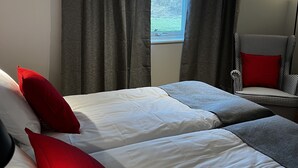 A bedroom with two beds, grey curtains, a window, a chair, and a floor lamp.