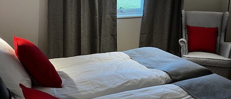 A bedroom with two beds, grey curtains, a window, a chair, and a floor lamp.