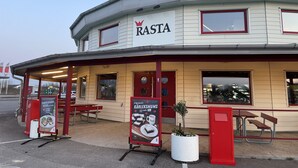 A building with a sign reading "RASTA" and a covered outdoor seating area with tables and benches.