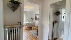 Un pasillo con radiador, suelo de madera y cestas colgantes con plantas.