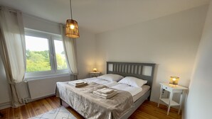 Un dormitorio con cama, dos lámparas de noche, una ventana, un radiador y una alfombra.