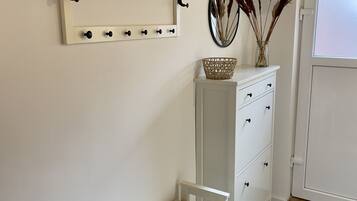 Une pièce avec un banc blanc, une commode blanche avec des tiroirs, un miroir avec des crochets et un panier posé sur la commode.