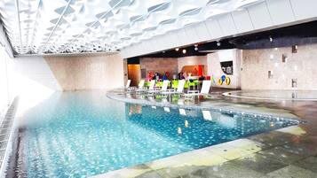 An indoor swimming pool with multiple lanes, lounge chairs, and a modern ceiling design.