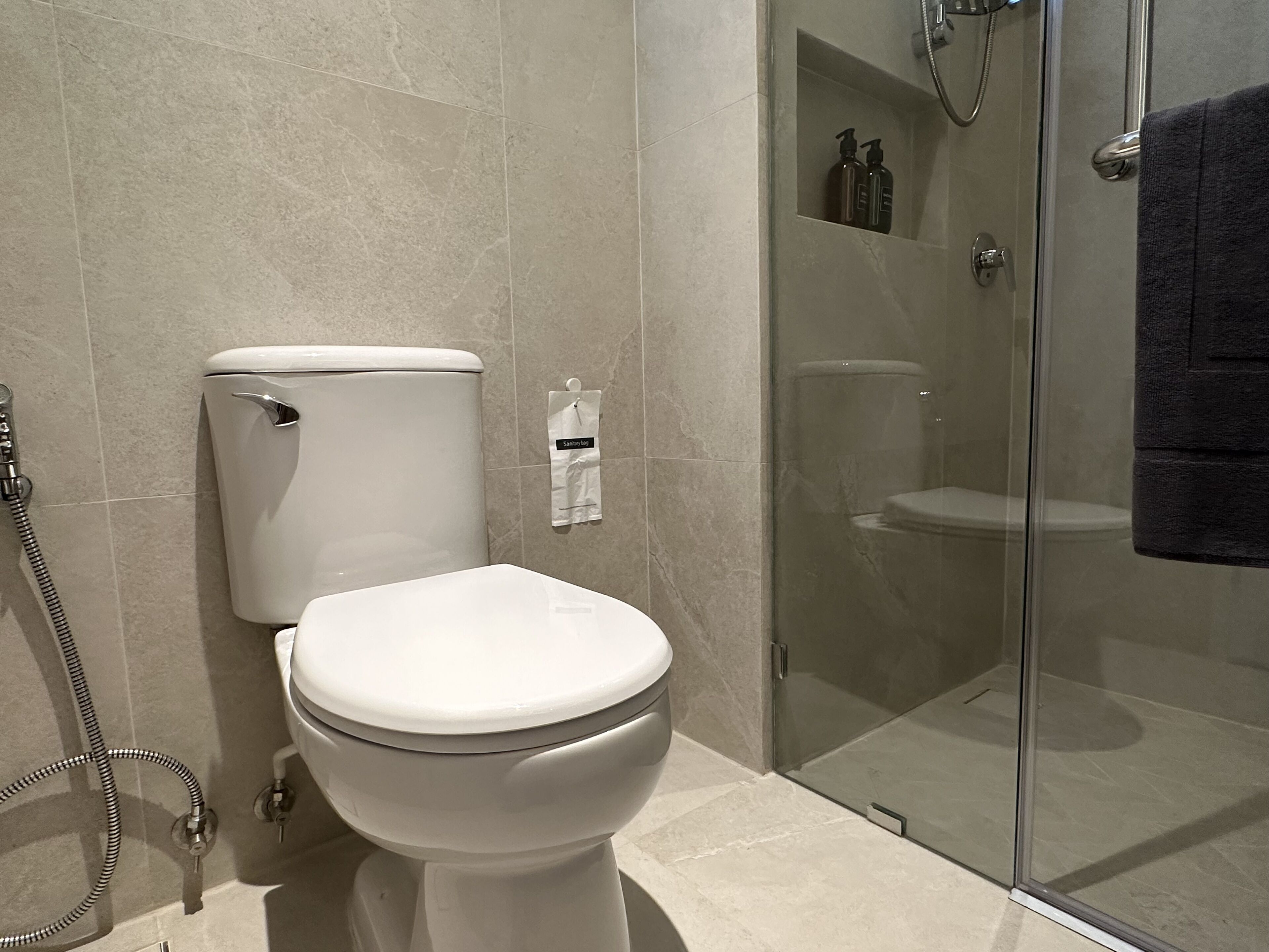 Un baño moderno con inodoro, cabina de ducha de vidrio y una toalla colgada en la puerta.