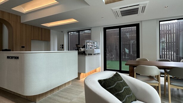 A modern reception area with a reception desk labeled "RECEPTION," a kitchen area with a coffee machine, and a dining area with a wooden table and chairs. - Jace Ratchada Hotel (Bangkok)