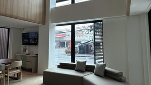 A spacious living area with a high ceiling, large windows, a comfortable seating area, and a flat-screen TV mounted on the wall. - Jace Ratchada Hotel (Bangkok)