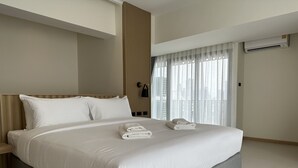 A modern hotel room with a large bed, a bedside table, a lamp, and a view of the city through sheer curtains. - Jace Ratchada Hotel (Bangkok)