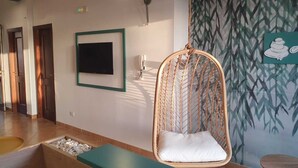 Een kamer met een hangstoel, een flatscreen televisie, een wandlamp en een decoratieve wand met een bamboepatroon.