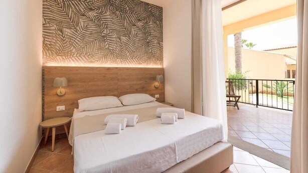 Een hotelkamer met een bed, nachtkastje, wandlamp en uitzicht op het balkon.