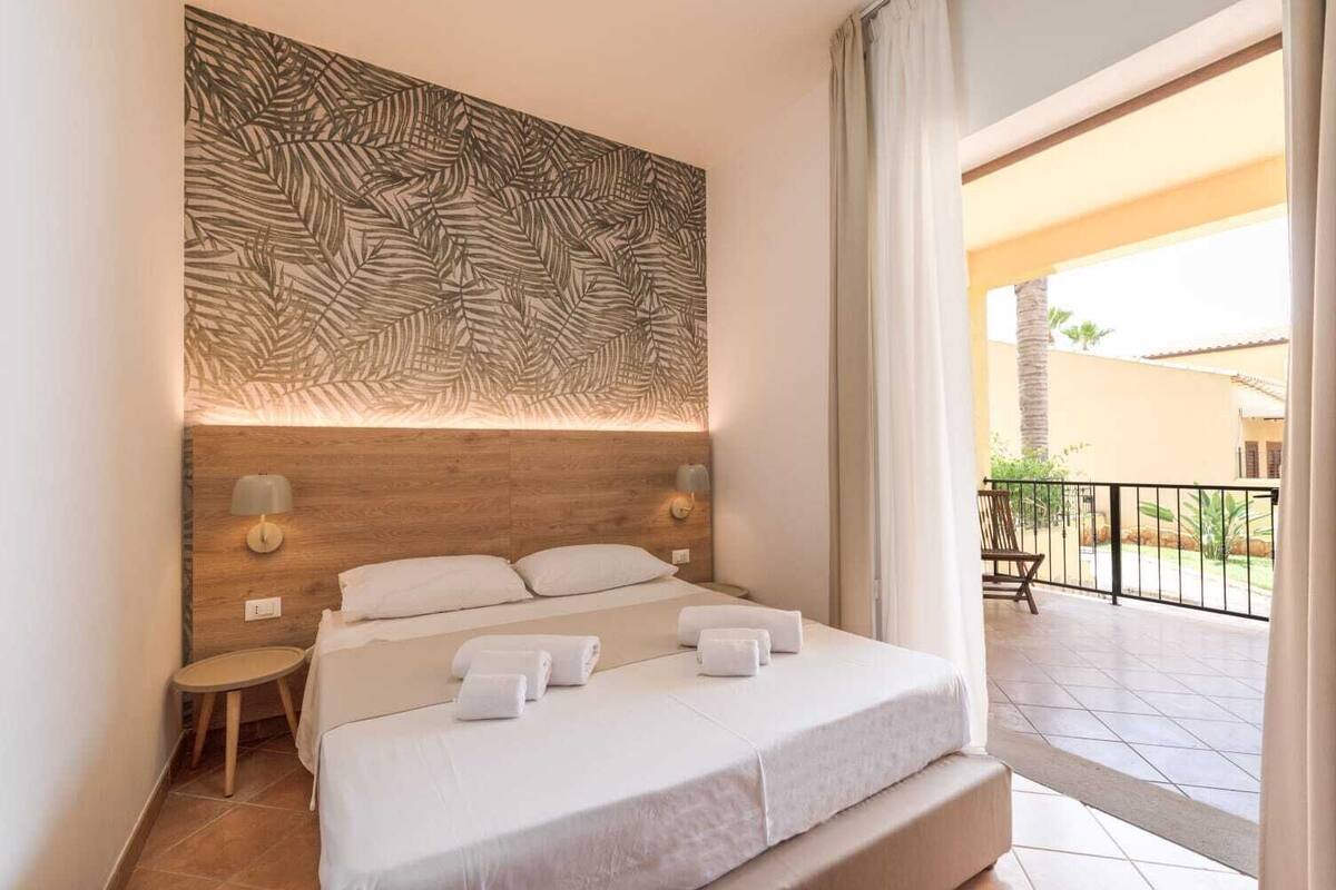 Een hotelkamer met een bed, nachtkastje, wandlamp en uitzicht op het balkon.