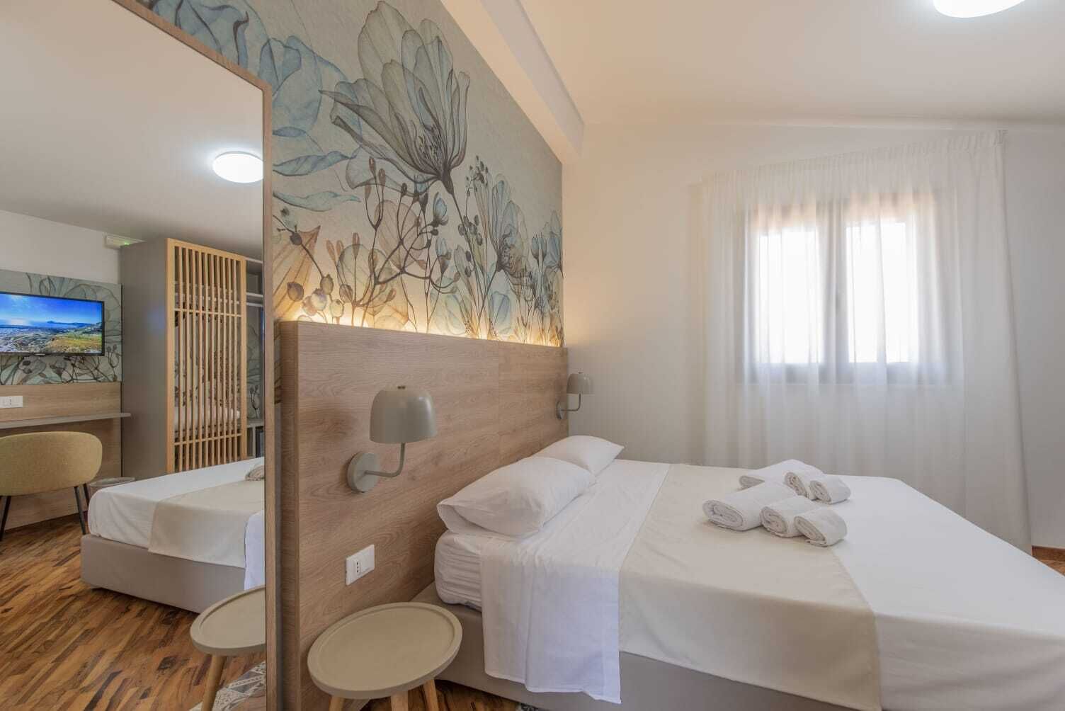 Habitación de hotel con cama, escritorio, silla, una mesita pequeña y un ventanal con cortinas.