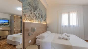 Habitación de hotel con cama, escritorio, silla, una mesita pequeña y un ventanal con cortinas.