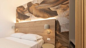 Een moderne hotelkamer met een houten hoofdbord, een bed met witte lakens, twee wandlampen en een klein rond tafeltje.