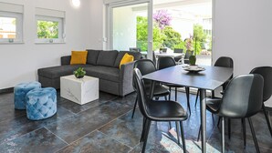 A modern living room with a grey sofa, blue ottomans, a white marble coffee table, and a dining area with a black table and chairs. - Villa for 20 with Private Pool  (Novalja)