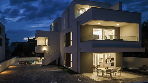 A modern two-story house with a balcony, outdoor seating, and a visible kitchen area. - Villa for 20 with Private Pool  (Novalja)
