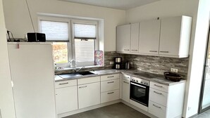 A modern kitchen with white cabinets, a built-in oven, and a window with blinds.