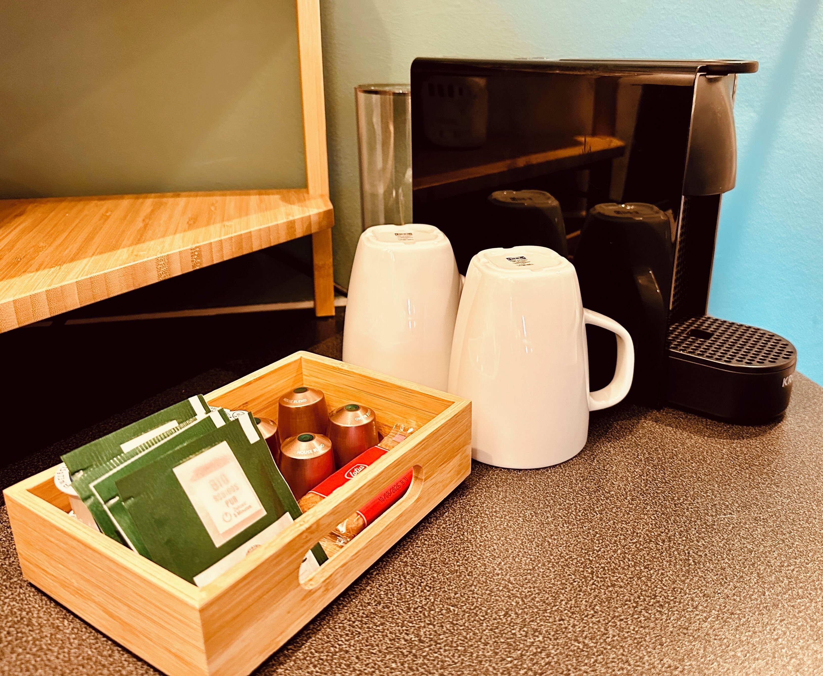 A kitchen area with a coffee maker, a kettle, and a wooden box containing tea bags and a tea kettle.
