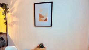 Uma área de refeições com uma mesa redonda de madeira, duas cadeiras, um quadro na parede e uma pequena planta sobre a mesa.