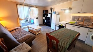 Espaço compacto para viver, com sofá, pequena mesa de jantar, cozinha equipada com frigorífico, fogão e pia.