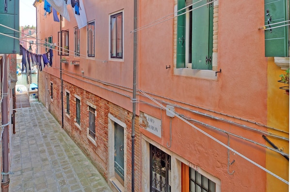 A narrow street with buildings on either side, featuring a sign that reads "RAMO AMON" and a visible door.