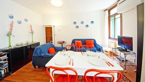 Een moderne woonkamer met een eettafel gedekt voor twee personen, een bank, een televisie en een boekenkast.