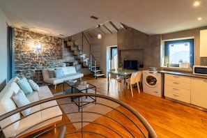 Een moderne woonkamer met een stenen muur, een trap, een bank, een eethoek en een keuken met een wasmachine.