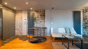 Un salon moderne avec un mur d’accent en pierre, une table ronde en métal, un canapé blanc agrémenté de coussins bleus et une porte grise.