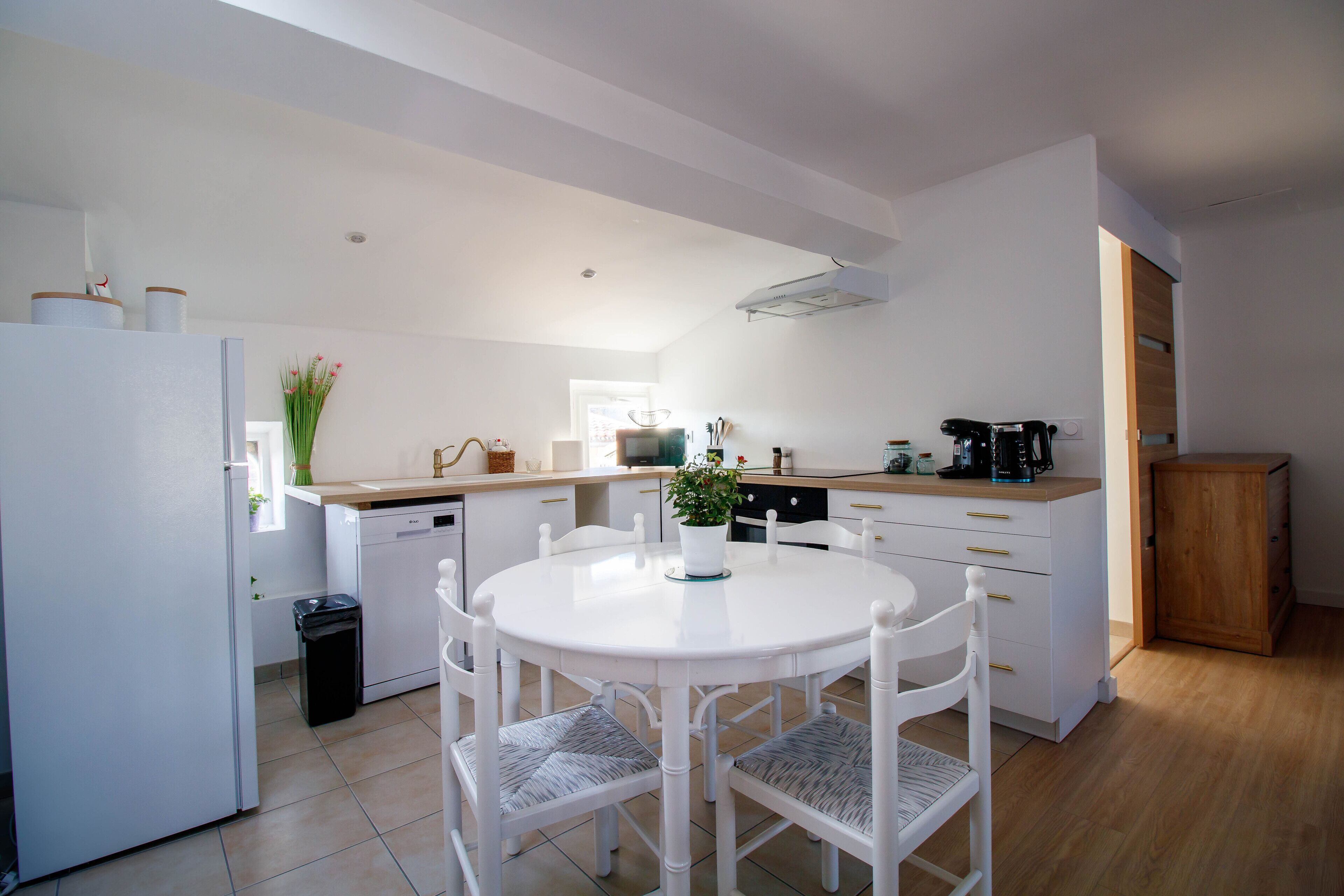 A modern kitchen with white cabinetry, a round dining table, and a coffee machine.