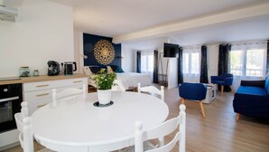 A modern living room with a white dining table, blue sofas, and a large decorative wall piece.