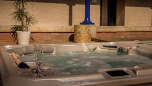 A hot tub with a champagne bottle and glass, surrounded by a brick wall and a potted plant.