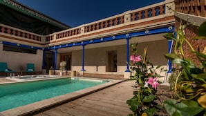 A pool area with a wooden deck, a hot tub, and a covered seating area with blue columns.