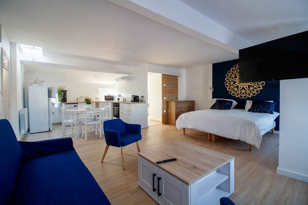 Una habitación moderna y bien iluminada con cama, sofá, zona de comedor y cocina.
