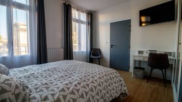 A hotel room with a bed, a desk, a chair, a TV, and a door.